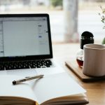 Laptop next to an open book on a desk